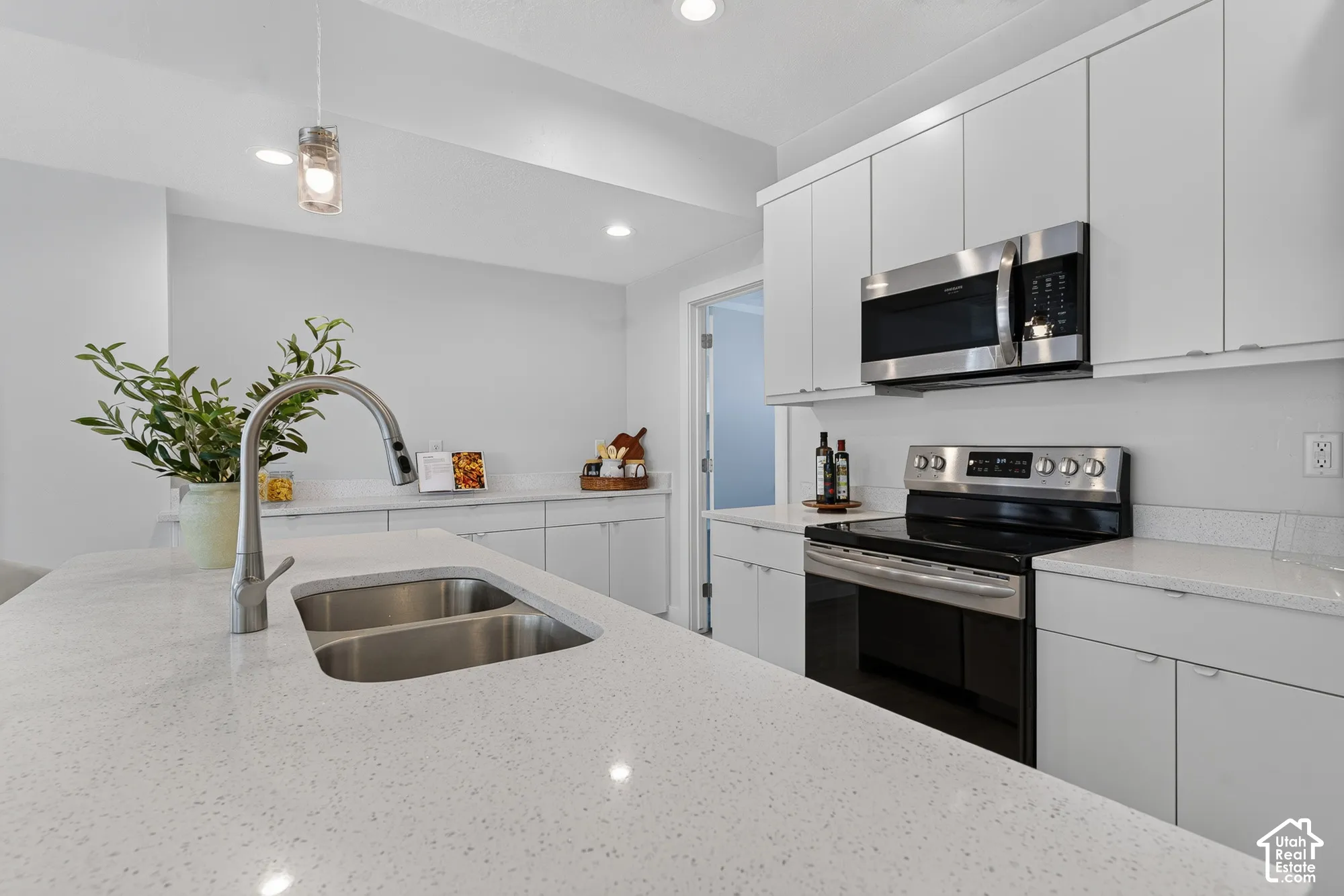 Contemporary kitchen featuring white cabinetry, light-toned countertops, stainless steel appliances, a double basin sink, and recessed lighting