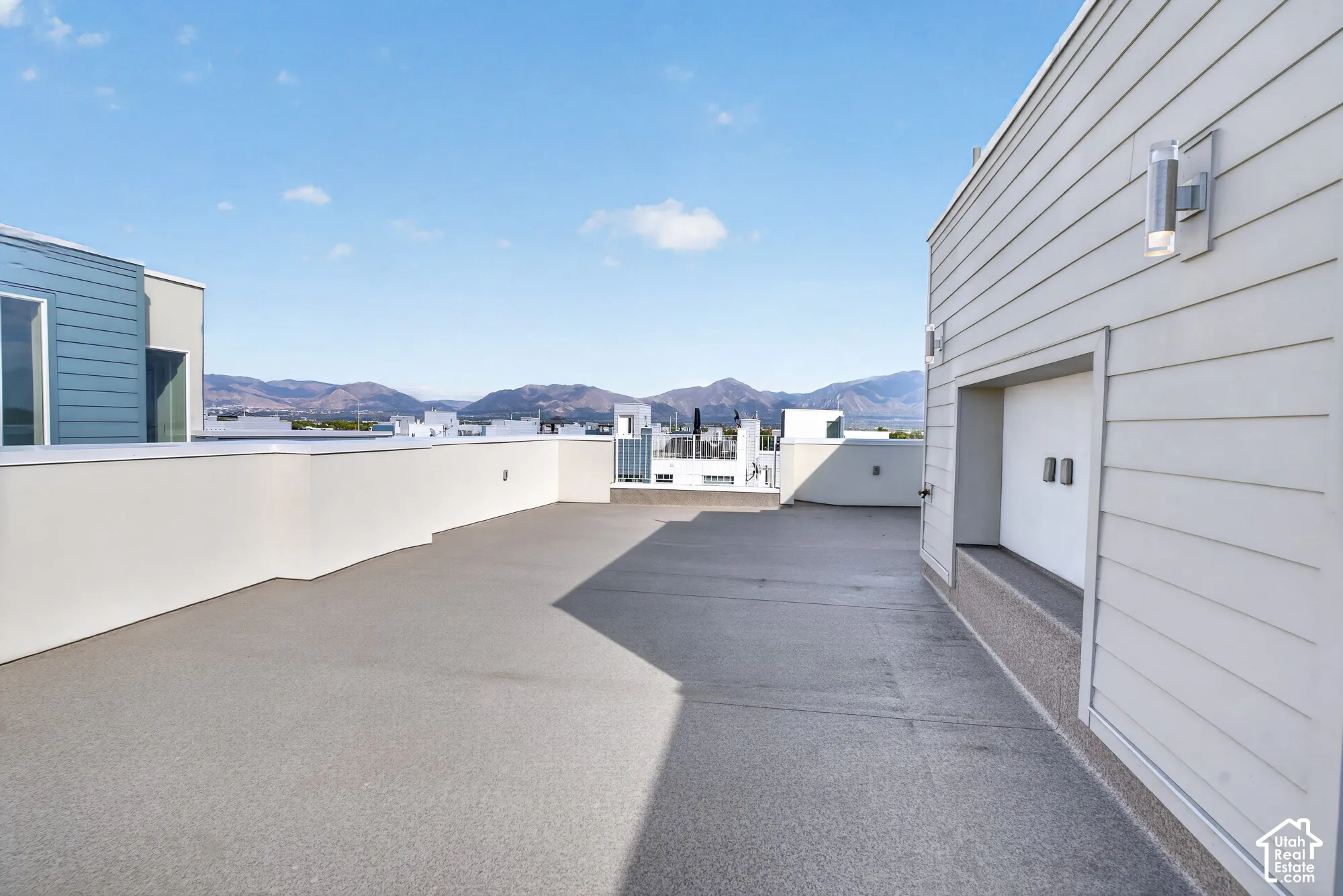 Expansive rooftop deck with mountain backdrop, featuring a low perimeter wall, light-toned wall siding, and modern exterior lighting fixtures