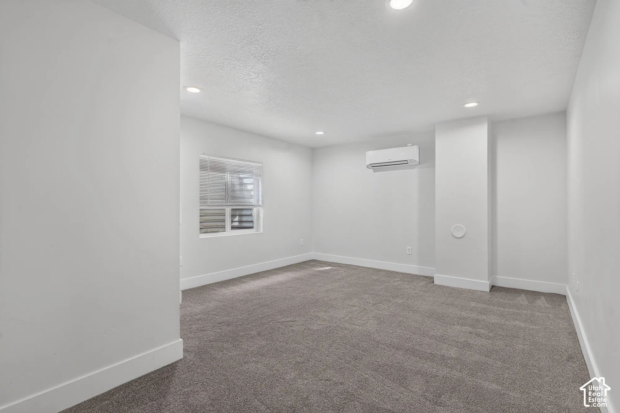 Recessed lighting, gray carpeting, white walls, window with blinds, and wall-mounted air conditioning unit