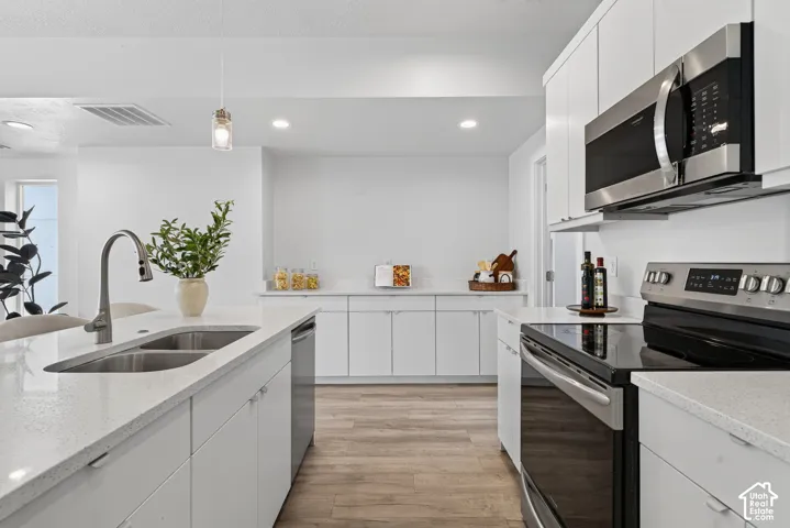 Kitchen featuring white cabinetry, light-toned countertops, stainless steel appliances, and wood-finish flooring