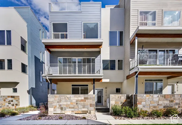 Contemporary facade with stone wall accents, multiple balconies, a rooftop deck, and a mix of siding and stucco finishes