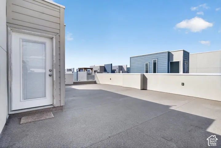 Expansive rooftop deck featuring a textured concrete surface, white plaster privacy walls, and modern exterior lighting fixtures