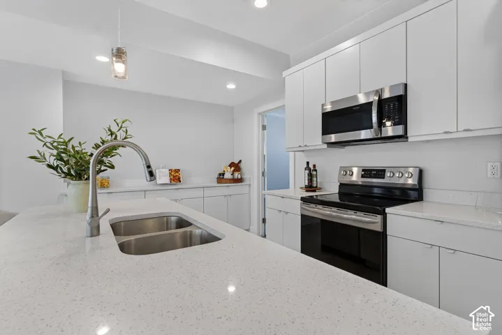 Contemporary kitchen featuring white cabinetry, light-toned countertops, stainless steel appliances, a double basin sink, and recessed lighting