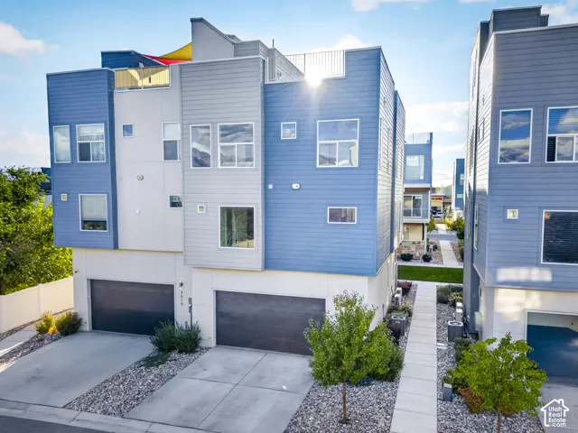 Contemporary multi-story exterior with varying shades of blue and gray siding, multiple windows, and a rooftop terrace