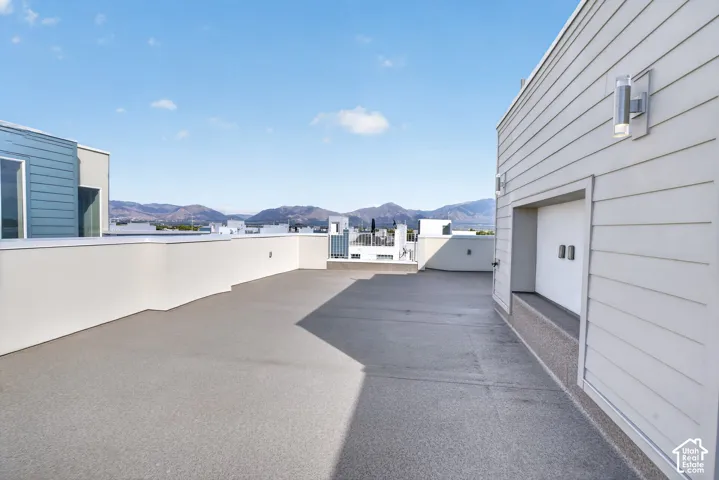 Expansive rooftop deck with mountain backdrop, featuring a low perimeter wall, light-toned wall siding, and modern exterior lighting fixtures