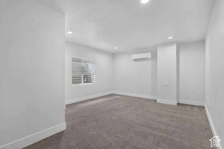 Recessed lighting, gray carpeting, white walls, window with blinds, and wall-mounted air conditioning unit