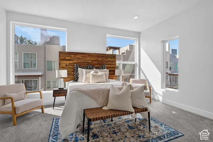 Recessed lighting, wood plank headboard, multiple large windows, and grey carpet flooring