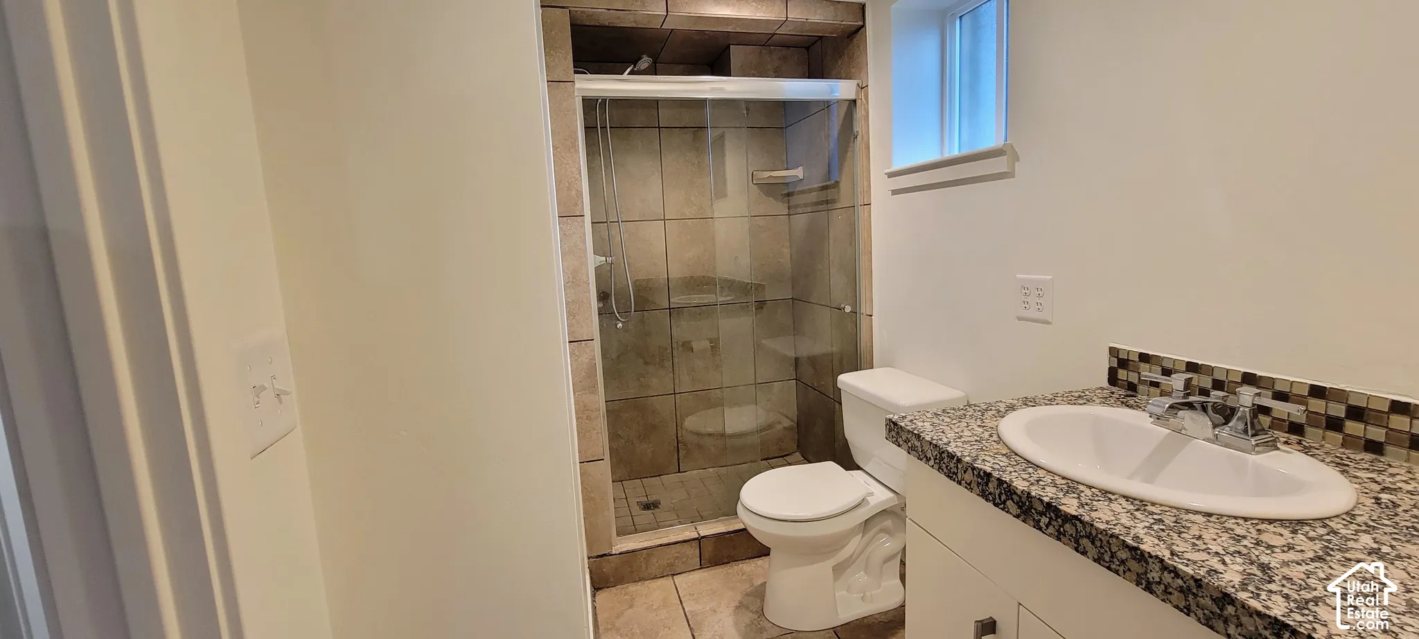 Tiled walk-in shower with clear glass enclosure, granite-style countertop, integrated sink, and mosaic tile backsplash