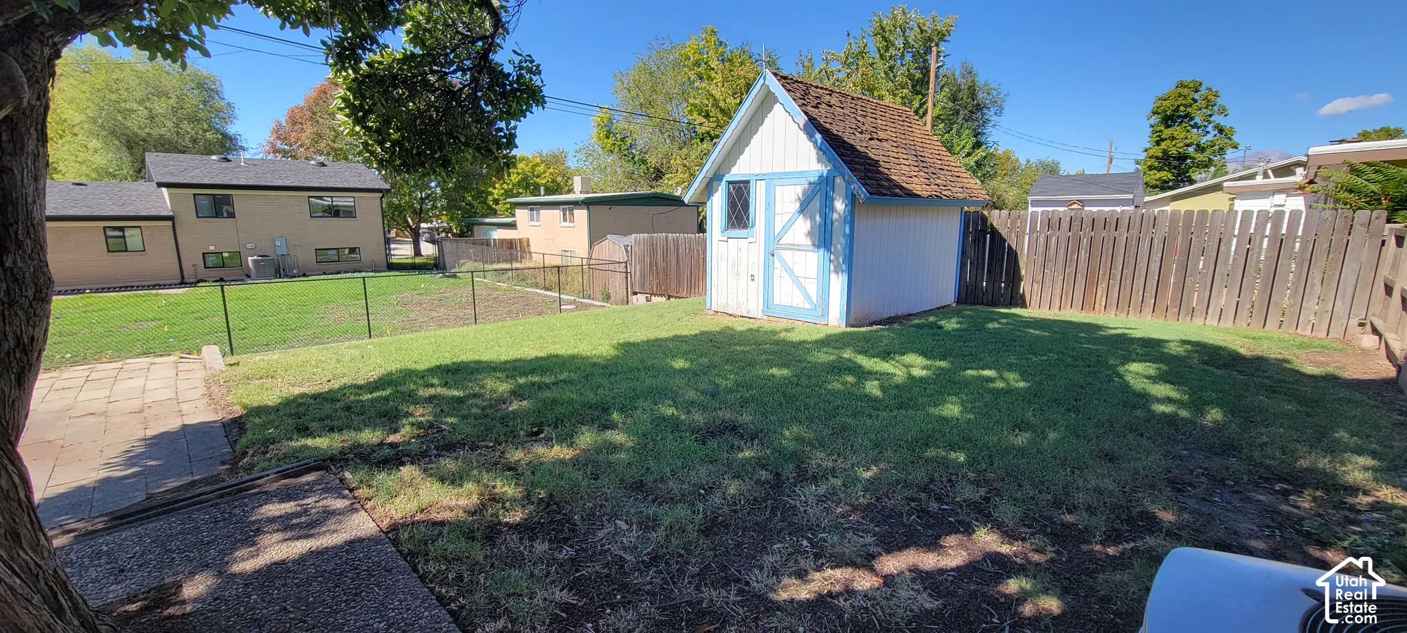 Expansive backyard featuring a storage shed with a shingle roof, a wood privacy fence, and a chain-link fence