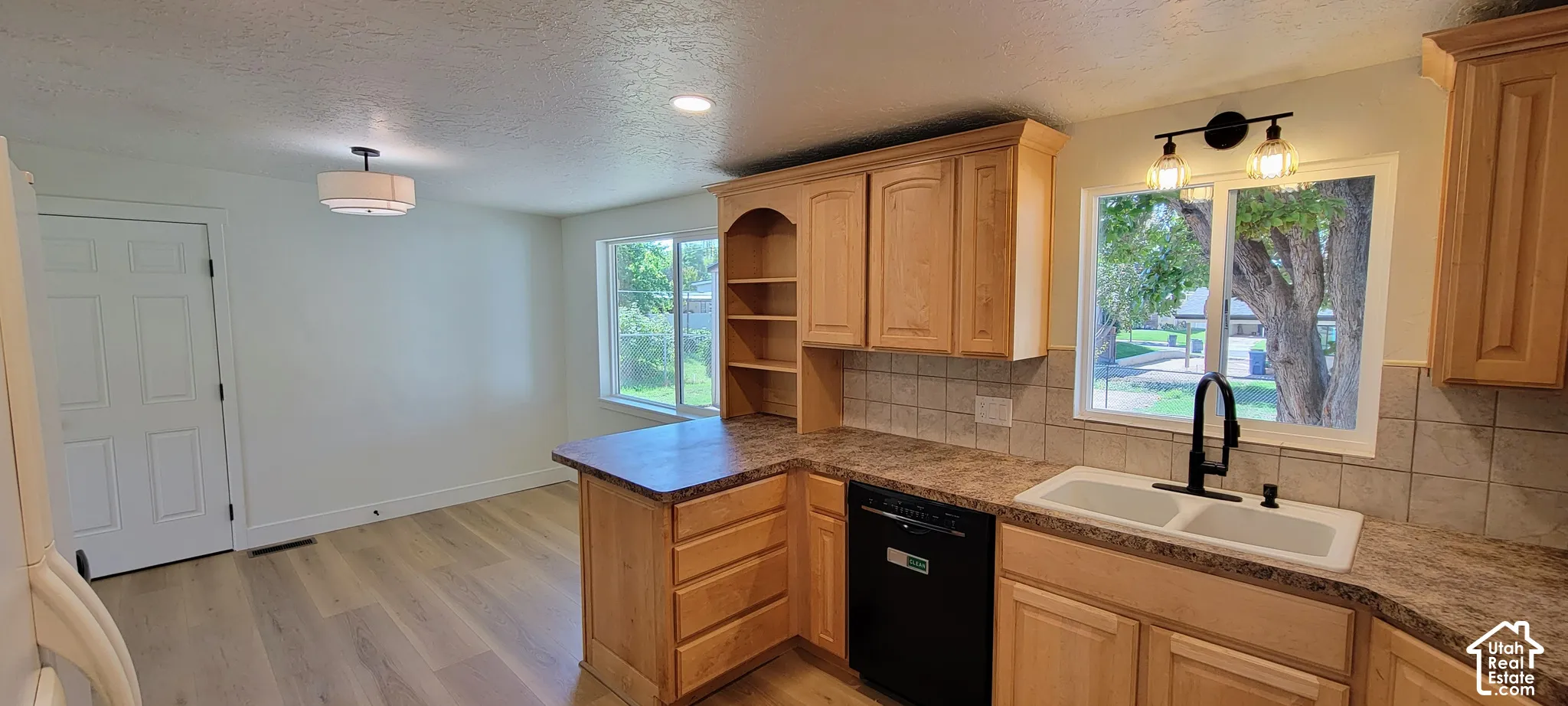 Wood-finish flooring, recessed lighting, double-basin sink with a matte black faucet, and light wood cabinetry with built-in shelving