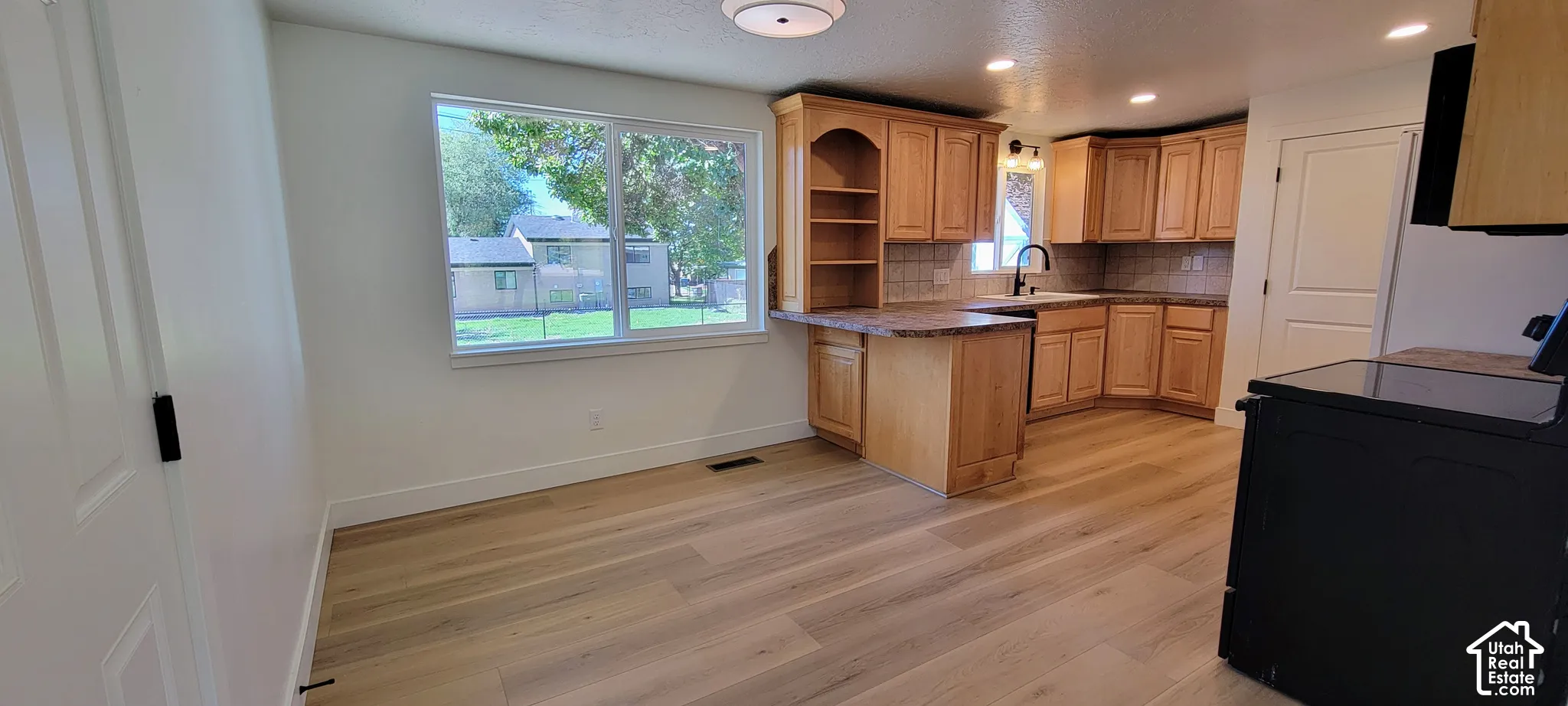 Kitchen featuring wood-finish flooring, light wood cabinetry, stone countertops, and a tile backsplash