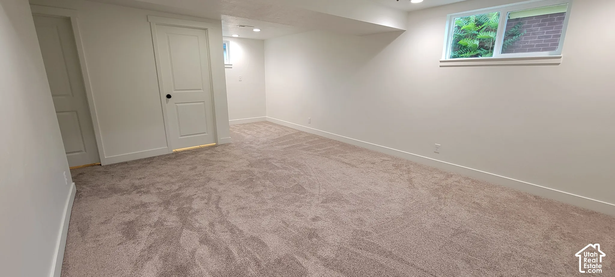 Expansive room with neutral carpeting, white walls, and a window providing natural light