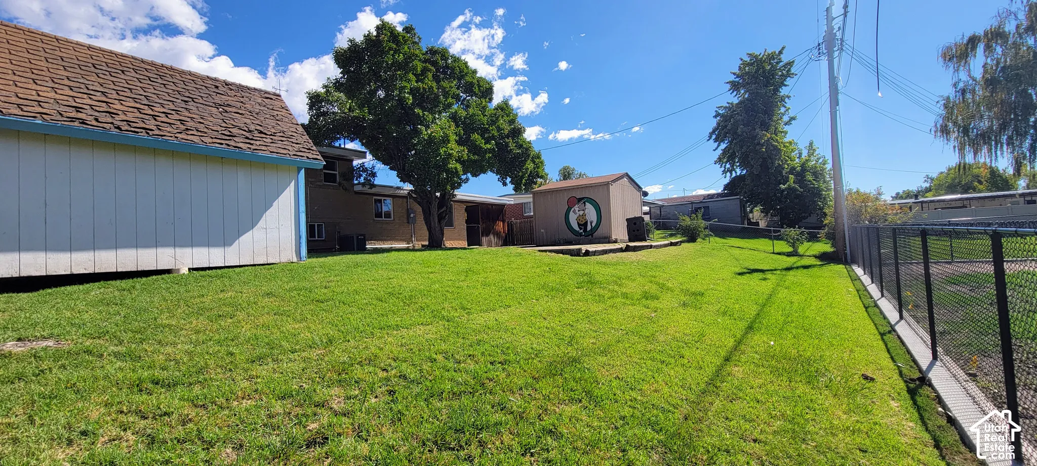 Expansive green lawn with a chain-link perimeter fence, detached storage shed, and mature trees