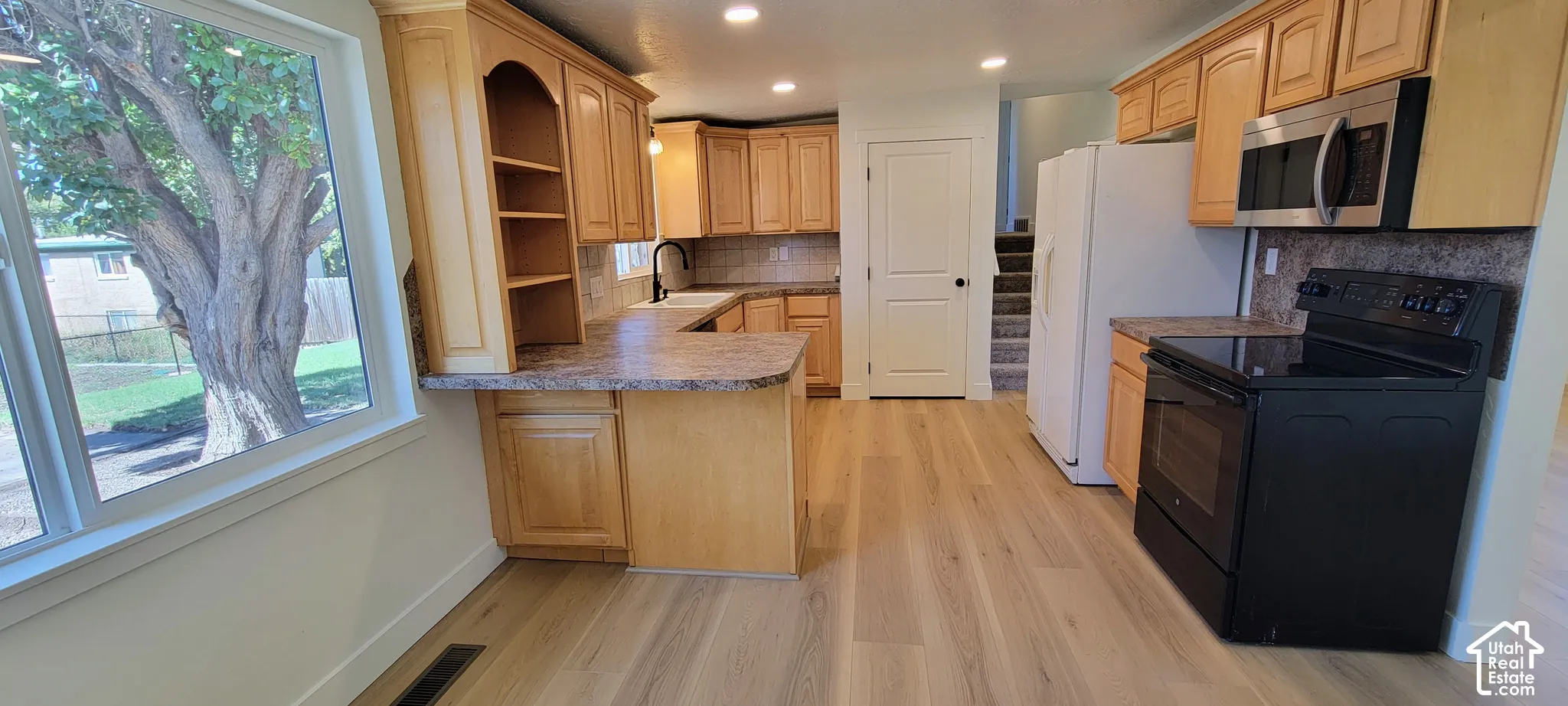 Kitchen featuring wood-finish flooring, light wood cabinetry, stone-look countertops, and stainless steel appliances