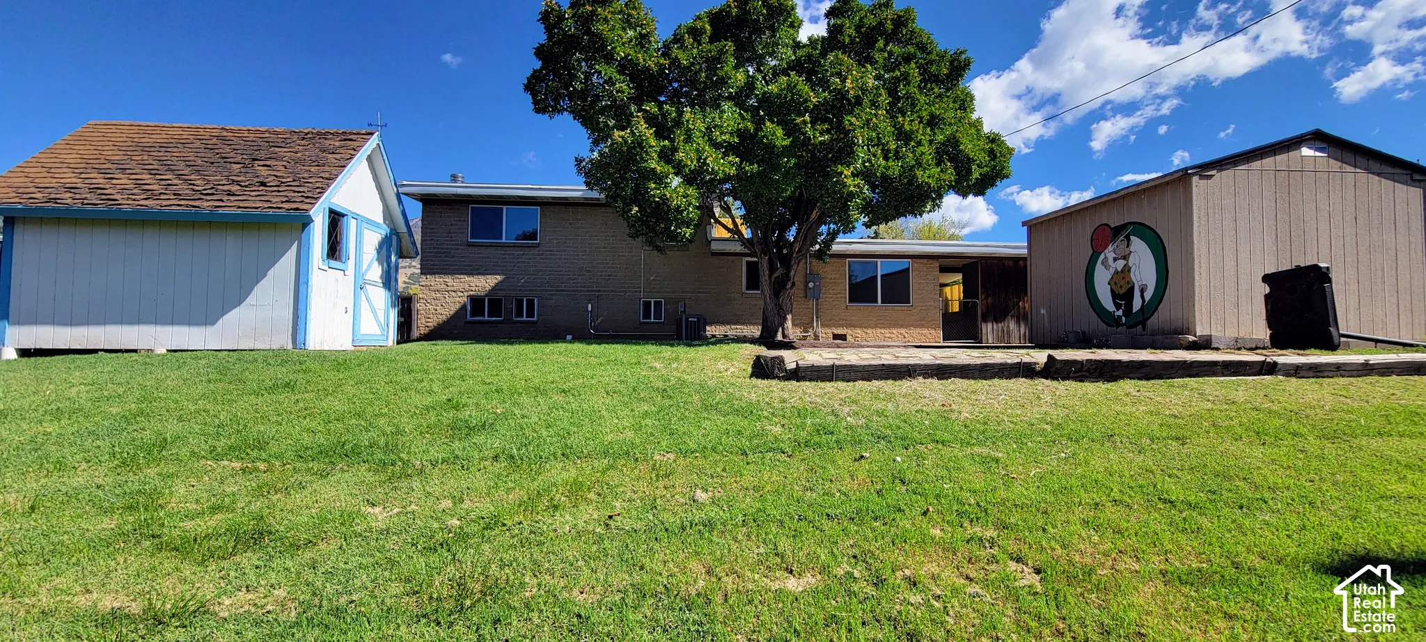 Expansive rear yard featuring green lawn, a large shade tree, and a concrete patio
