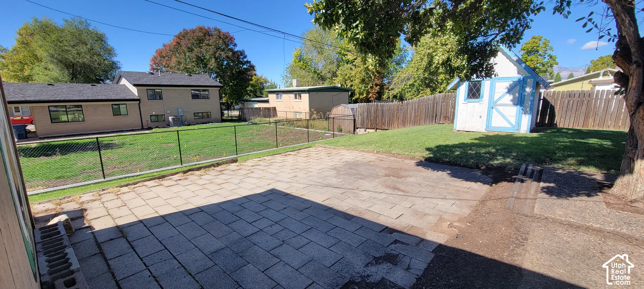 Expansive backyard featuring a paver patio, chain-link fencing, a wooden privacy fence, a storage shed, and a grassy lawn