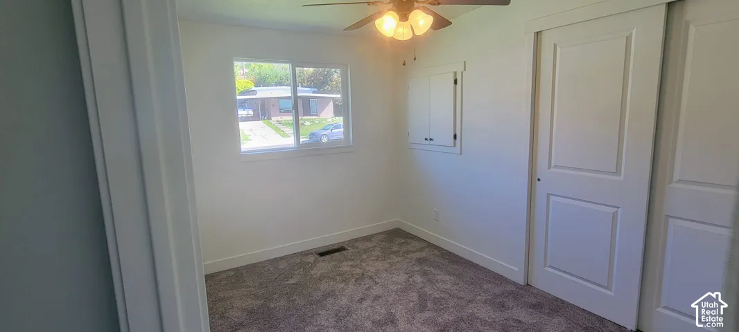 Room featuring carpet flooring, a window with white trim, a ceiling fan with integrated lighting, and a built-in wall cabinet