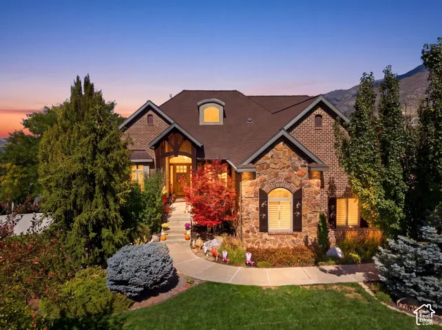 Stone and brick exterior with arched windows, prominent front entrance, dormer window, and mature landscaping