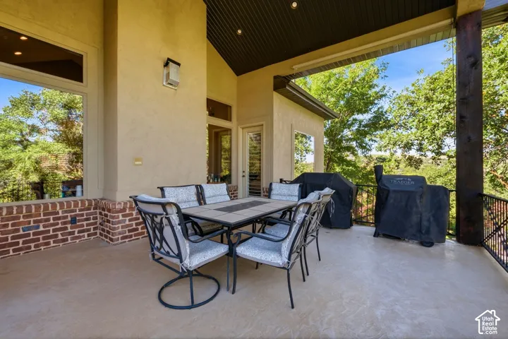 Expansive covered patio featuring a high vaulted ceiling, stucco exterior, brick half-wall, and wrought iron railing