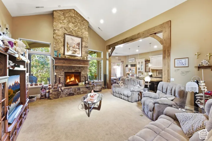 Vaulted ceiling with recessed lighting, stone fireplace with a wood mantel, expansive windows, and a wood-beam entryway