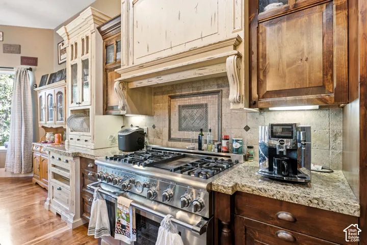 Stainless steel range with multiple burners, stone countertops, tiled backsplash with decorative inlay, and distressed wood-finish cabinetry