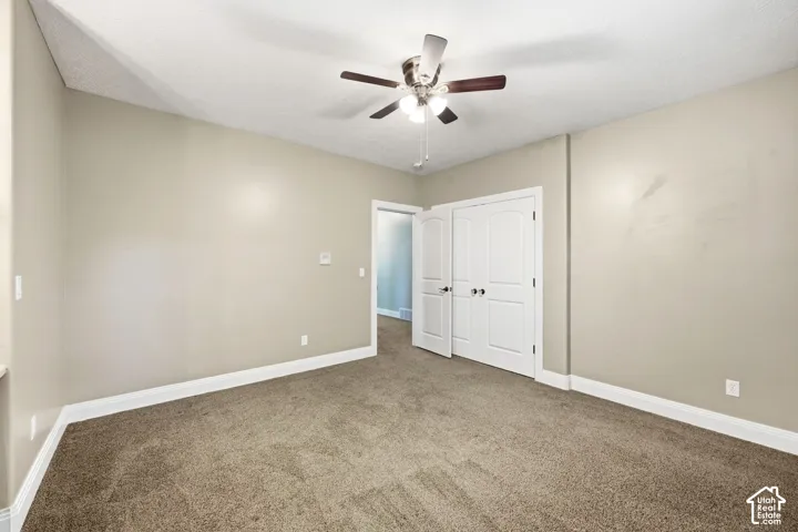 Carpeted room featuring a ceiling fan with light fixture, double closet doors, and white trim