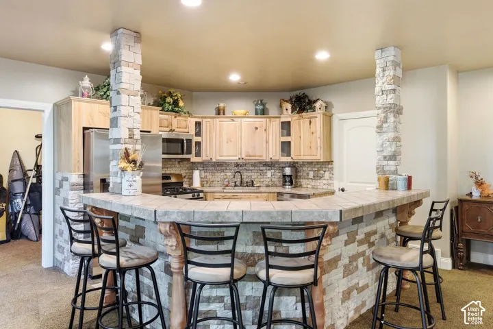 Kitchenette with a tiled breakfast bar, stacked stone accents, recessed lighting, wood cabinetry, and stainless steel appliances
