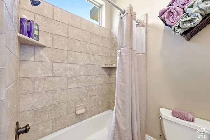 Bathtub with subway tile surround, built-in shelving, and a dark bronze shower fixture
