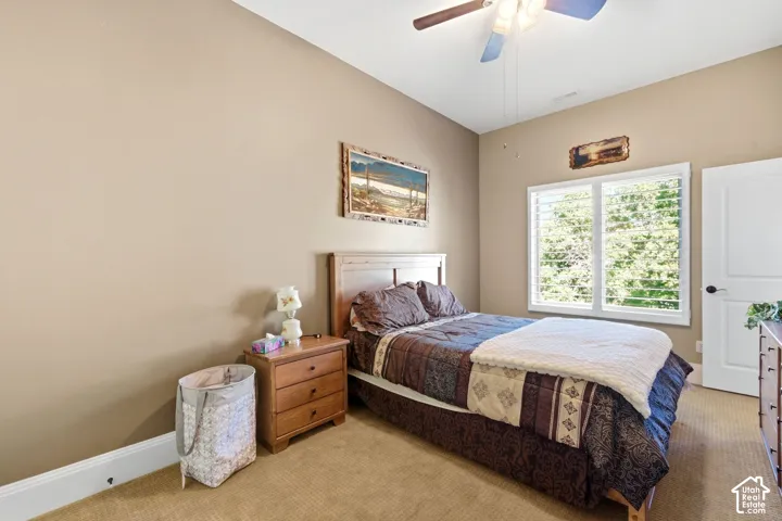 Recessed ceiling light, ceiling fan with integrated lighting, wood-finish headboard, window with plantation shutters, wood-finish nightstand