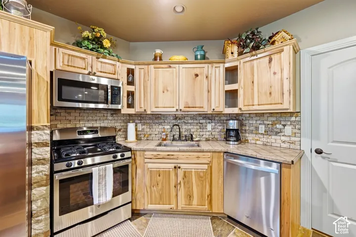 Kitchen featuring wood-finish cabinetry, stainless steel appliances, a tiled backsplash, and stone countertops