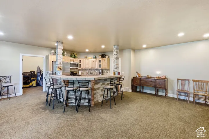 Full kitchen with light wood-finish cabinetry, stainless steel appliances, and a stone-clad island