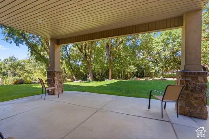Covered patio with stone-clad columns and a concrete surface, opening to a grassy yard with mature trees
