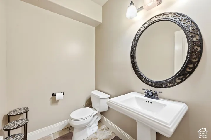 Pedestal sink with dual-handle faucet, decorative round mirror, and tile flooring