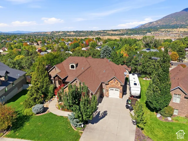 Stone and brick exterior with dormer windows, a concrete driveway, two-car garage, and established landscaping