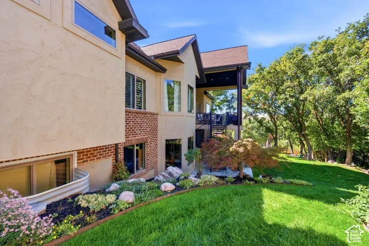Multi-story exterior featuring stucco and brick finishes, a covered deck with a spiral staircase, and a landscaped garden bed with mature trees