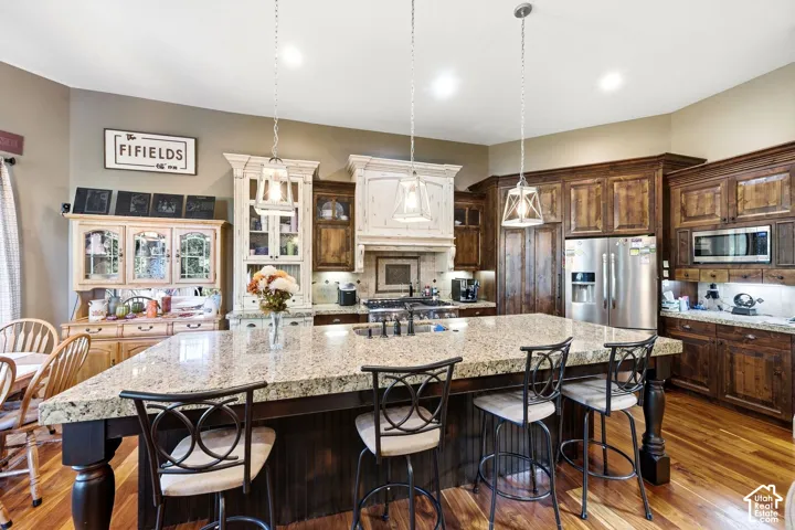 Granite island with integrated seating, hardwood flooring, and stainless steel appliances