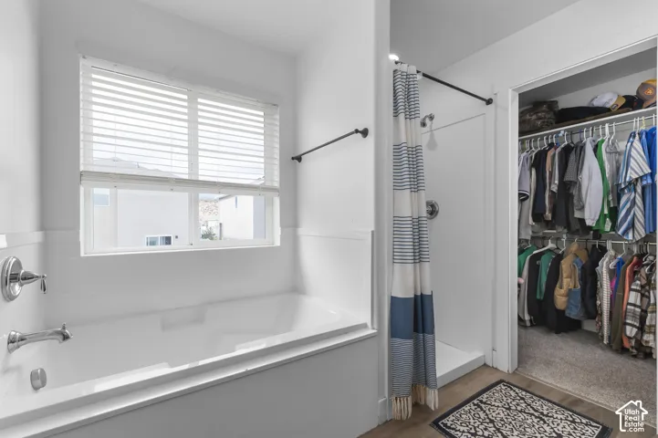 Built-in bathtub with chrome fixtures, window with blinds, stand-up shower, and organized closet with shelving