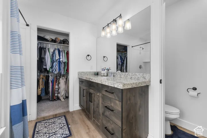 Wood-finish flooring, dark wood vanity with ample storage, light speckled countertop, large wall-mounted mirror, and a wall-mounted light fixture with five individual lights