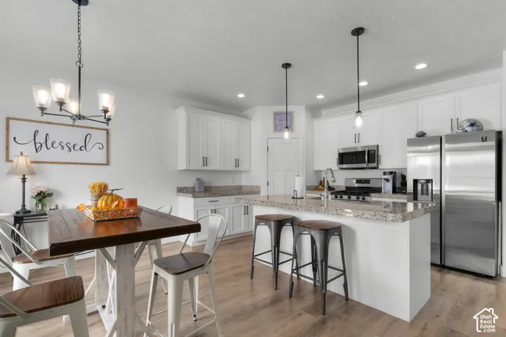 White shaker cabinetry, stainless steel appliances, granite countertops, wood-finish flooring, and pendant lighting
