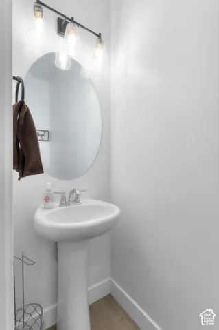 Pedestal sink with chrome fixtures, oval wall-mounted mirror, and a three-light vanity bar