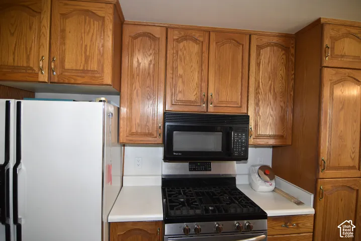 Wood-finish cabinetry with decorative panels, white solid surface countertops, a stainless steel range, and a black microwave