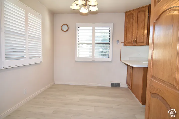 Light wood-finish flooring, white wall paint, two windows with white plantation shutters, built-in wooden cabinetry, and white countertops