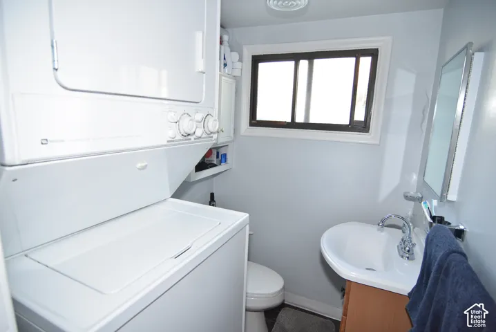 ADU private Stackable laundry machines, white wall-mounted sink, wood-finish vanity with chrome faucet, framed mirror, toilet and a window with dark trim