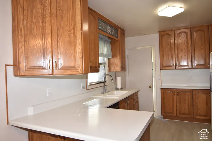 Wood-finish cabinetry, white countertops, stainless steel sink, flat panel lighting, and wood-finish flooring