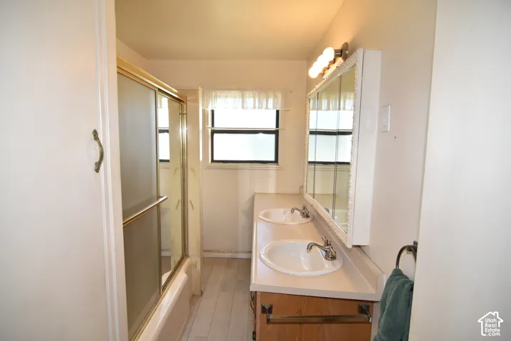 Main upstairs bathroom with Double vanity with two sinks, wall-mounted light fixture, and a tub-shower combination with sliding glass doors