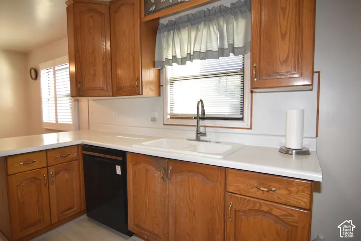 Wood-finish cabinetry, white countertops, built-in dishwasher, stainless steel faucet, and a dual-basin sink