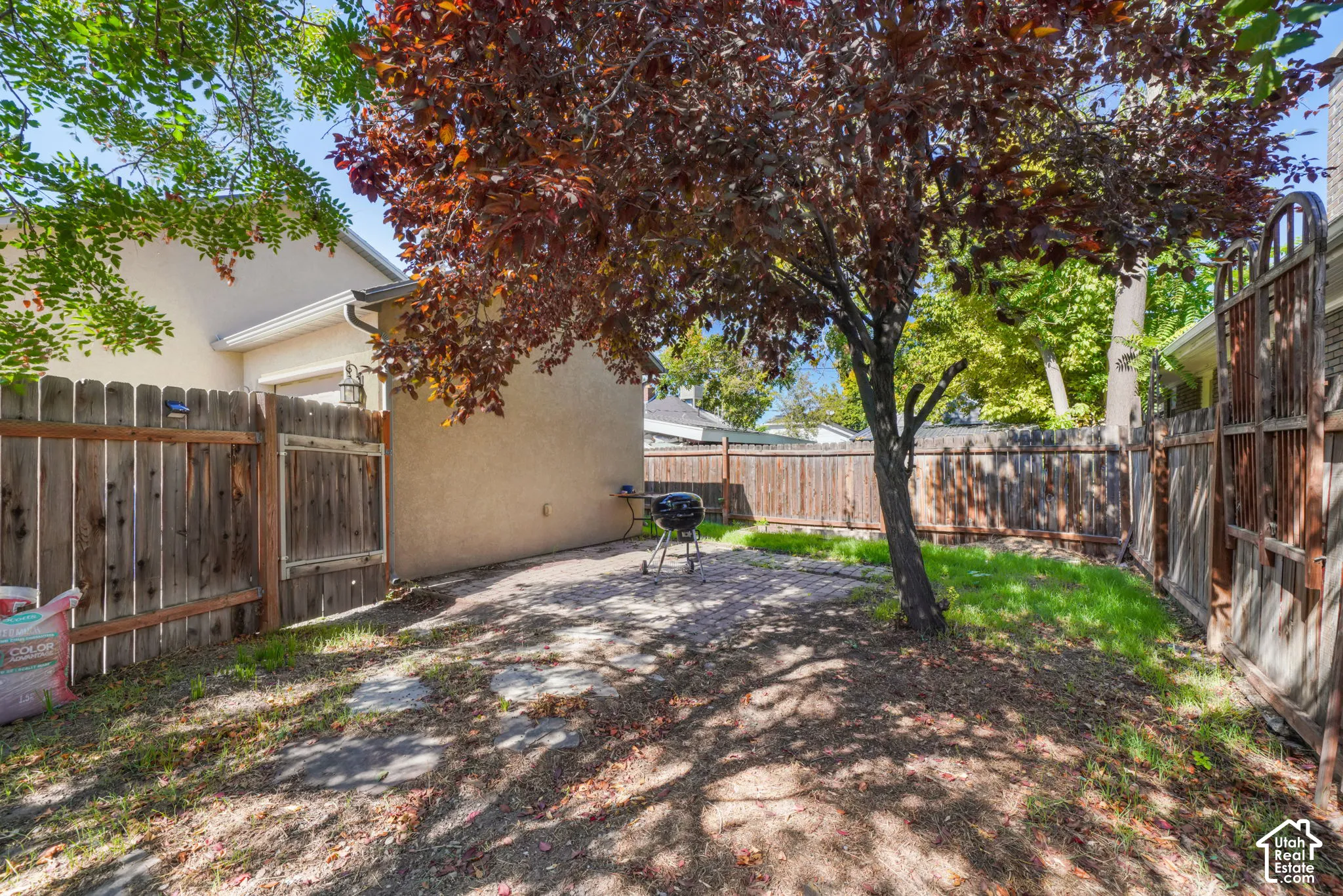 Fenced backyard with mature tree, a paved patio area, and a grass section