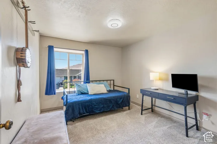 Carpeted room featuring a window with natural light, textured ceiling, and a ceiling-mounted smoke detector
