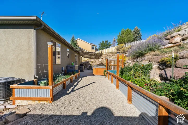 Terraced backyard featuring a gravel pathway, raised garden beds, and a built-in spa