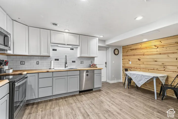Kitchen featuring wood-finish flooring, two-tone cabinetry, wood countertops, a subway tile backsplash, and a built-in dishwasher